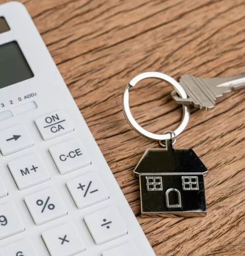 Clé de maison avec porte-clés de maison ou porte-clés avec calculatrice blanche sur table en bois utilisée comme calcul d'hypothèque ou achat et vente de propriétés et de biens immobiliers.