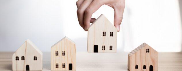 Un homme d'affaires tenant une maison en bois sur une table symbolise l'investissement immobilier, le choix de la meilleure maison pour un investissement à long terme